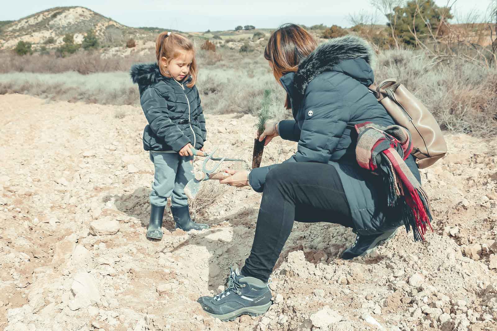Una mujer y un niño están al aire libre, plantando un joven árbol en un paisaje seco.