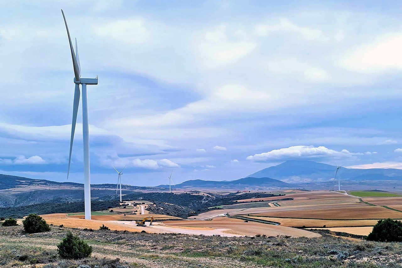 Un paisaje escénico con múltiples aerogeneradores frente a colinas onduladas y un cielo nublado.