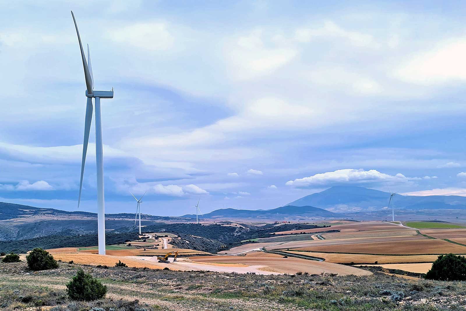 Un paisaje escénico con múltiples aerogeneradores frente a colinas onduladas y un cielo nublado.