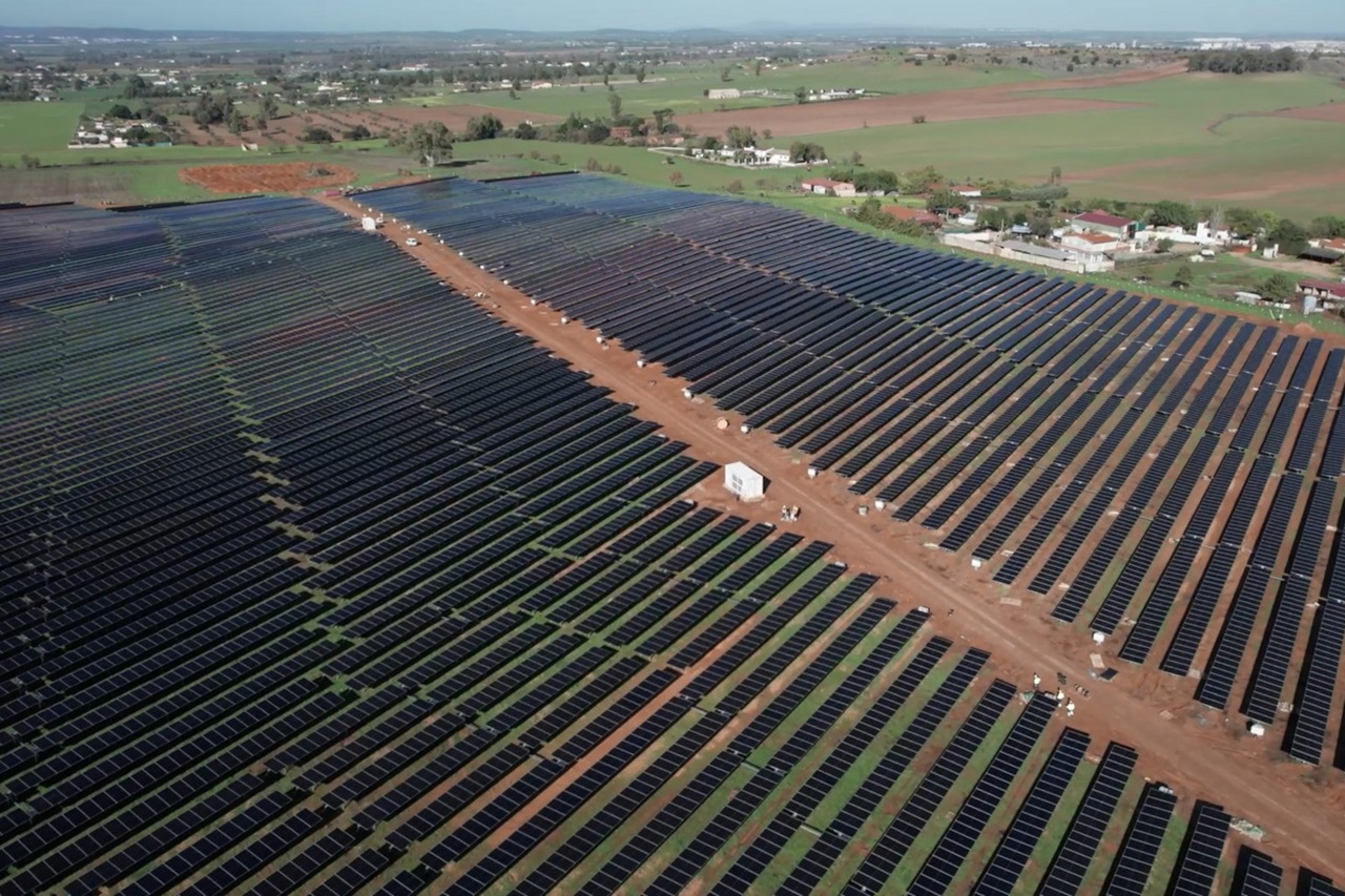 Vista aérea de una extensa planta solar con filas de paneles solares que se extienden a través de campos verdes.