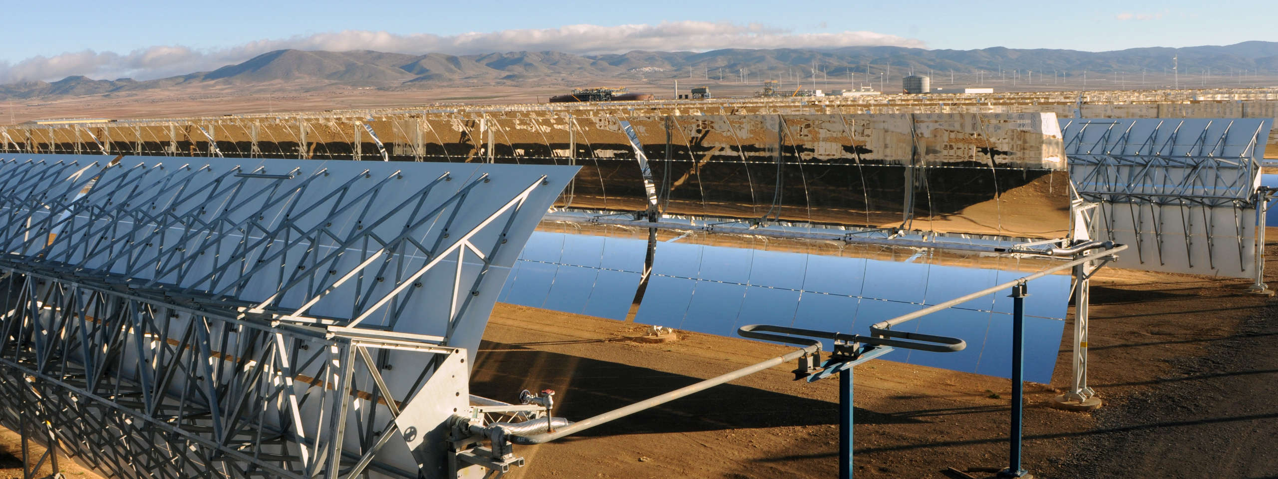 A solar energy facility featuring reflective collectors capturing sunlight, with mountains visible in the background.