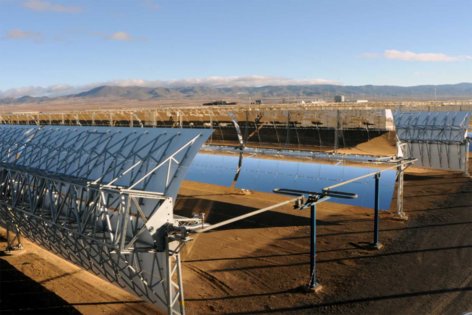 A solar power plant featuring large curved mirrors reflecting sunlight towards a central tower under a clear blue sky.