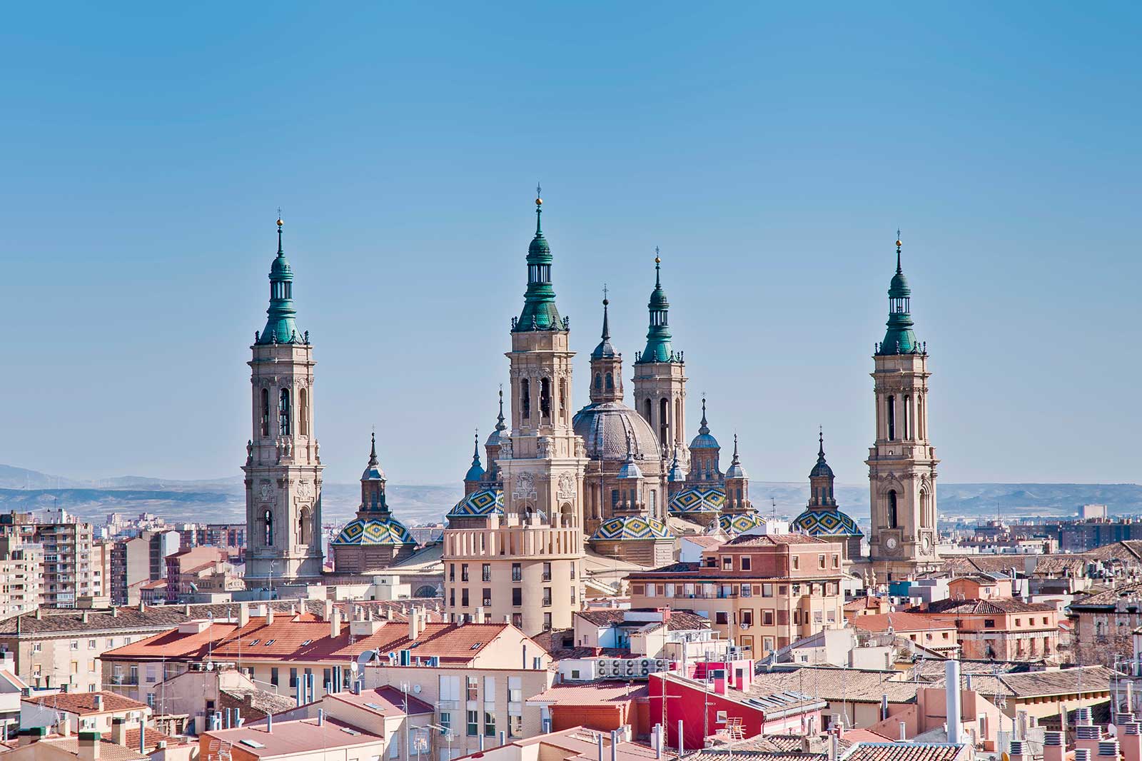 Una vista panorámica del horizonte de Zaragoza con la Basílica del Pilar y edificios circundantes bajo un cielo azul claro.