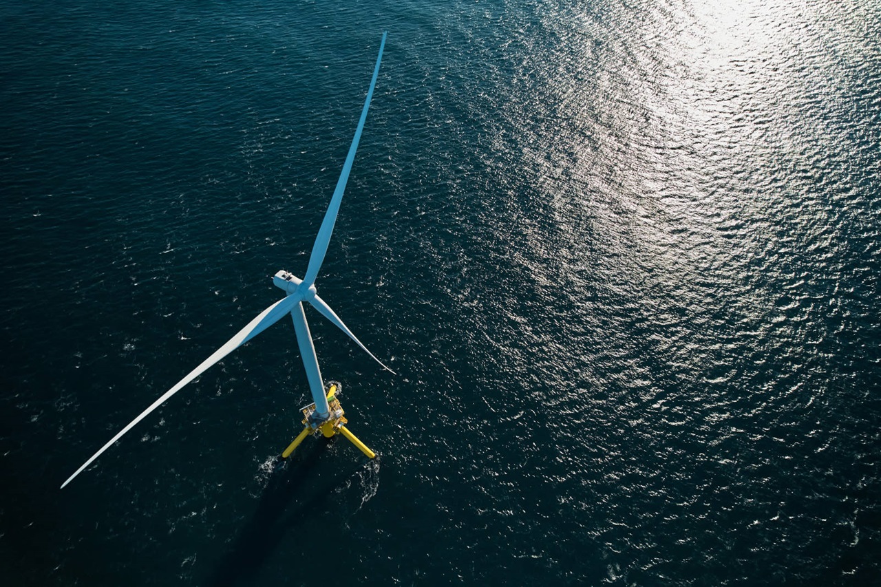 Una vista aérea de un gran aerogenerador sobre un mar azul, con ondas brillantes que reflejan la luz del sol.